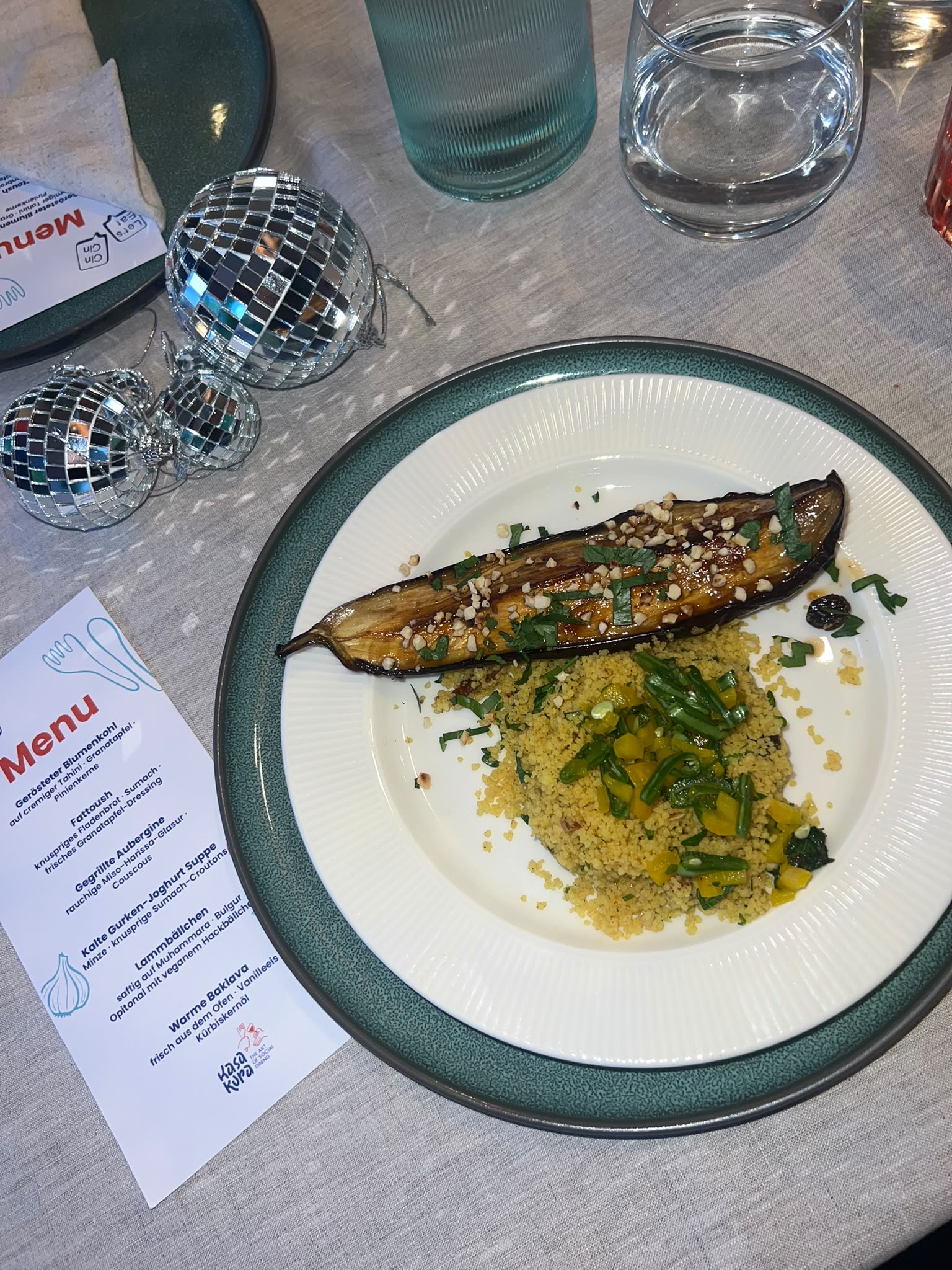 Gegrillte Aubergine mit Miso-Harissa-Glasur auf Couscous, daneben die Menükarte